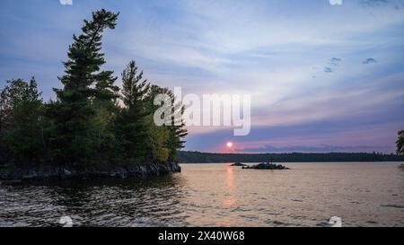 Malerischer Sonnenuntergang über einem See mit einem rosa Sonnenstrahl reflektiert auf dem ruhigen Wasser; Lake of the Woods, Ontario, Kanada Stockfoto