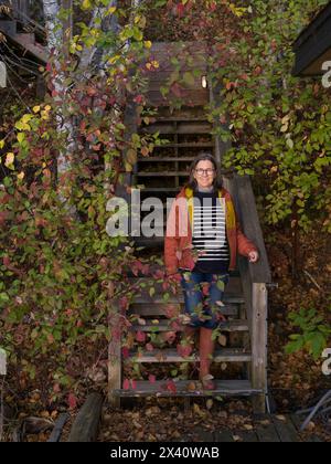 Frau steht auf Holztreppen im Freien, umgeben von Herbstlaub; Lake of the Woods, Ontario, Kanada Stockfoto