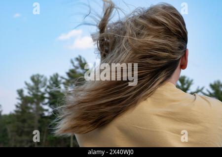 Mädchen steht draußen mit ihrem T-Shirt und langen Haaren, die im Wind wehen; Lake of the Woods, Ontario, Kanada Stockfoto