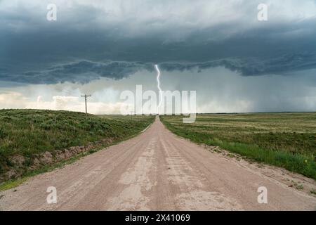 Ein Blitz trifft von einem Gewitter, während eine einsame Straße in den Sturm führt: Kansas, Vereinigte Staaten von Amerika Stockfoto