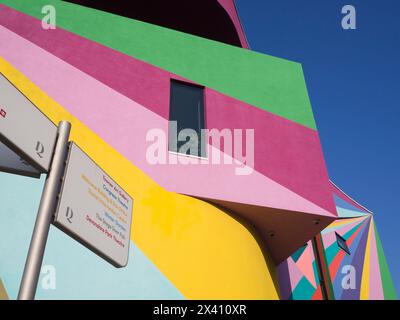 Außenwände einer Kunstgalerie in leuchtenden Farben vor einem blauen Himmel und einem Wegweiser mit einer Liste lokaler Sehenswürdigkeiten Stockfoto