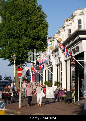 Leute, die draußen an Tischen sitzen und auf der Carlisle Road spazieren gehen, mit Union Jacks fliegen, Eastbourne, East Sussex, Großbritannien; Eastbourne, East Sussex, England Stockfoto