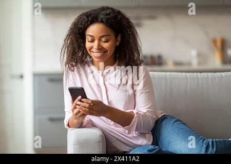 Inhalt Junge Schwarze Frau, die zu Hause auf der Couch schreibt Stockfoto
