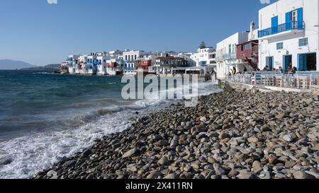 Historische Fischerhäuser in Little Venice, mit einer Terrasse am Wasser und einem Felsenstrand im Vordergrund auf der Insel Mykonos Stockfoto