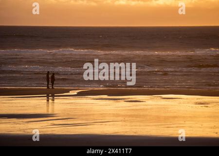 Paare beobachten den Sonnenuntergang über dem Pazifik vom Strand im Cape Disappointment State Park nahe der Mündung des Columbia River, Washington ... Stockfoto