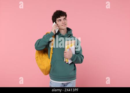 Porträt eines Schülers mit Rucksack und Notizbüchern, die am Telefon sprechen, vor rosa Hintergrund Stockfoto