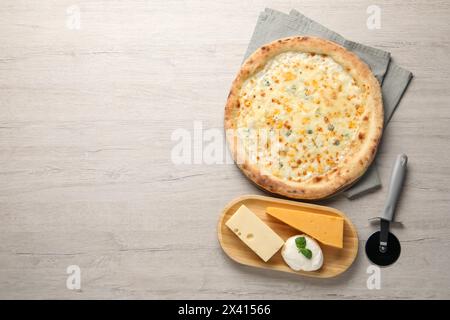 Leckere Käsepizza, Cutter und verschiedene Käsesorten auf Holztisch, flach gelegen. Leerzeichen für Text Stockfoto