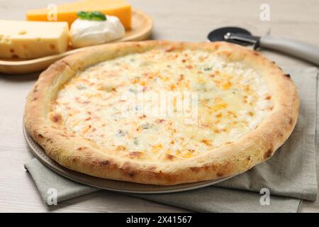 Leckere Käsepizza, Cutter und verschiedene Käsesorten auf Holztisch, Nahaufnahme Stockfoto