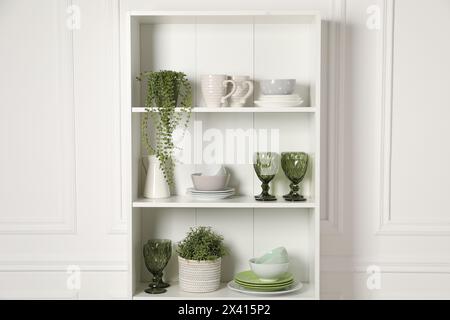 Verschiedene saubere Geschirr und Zimmerpflanzen auf den Regalen im Schrank drinnen Stockfoto