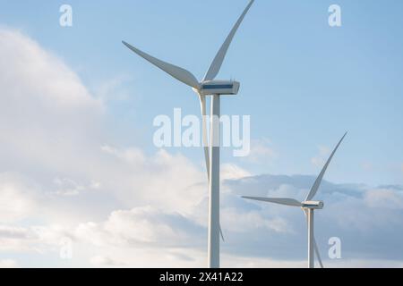 Zwei Windenergieanlagen stehen hoch am Himmel, von denen eine höher ist als die andere. Der Himmel ist bewölkt, aber die Sonne ist immer noch sichtbar, Kreatin Stockfoto