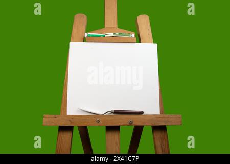 Eine Leinwand auf Malerei Staffelei mit Palettenmesser, Spachtel und Farbe für Malerei, künstlerische Materialien auf grünem Hintergrund. Stockfoto