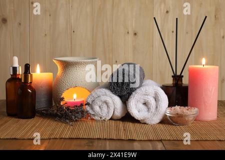 Aromatherapie. Duftende Kerzen, Flaschen, Lavendel, Handtücher und Meersalz auf Holztisch Stockfoto