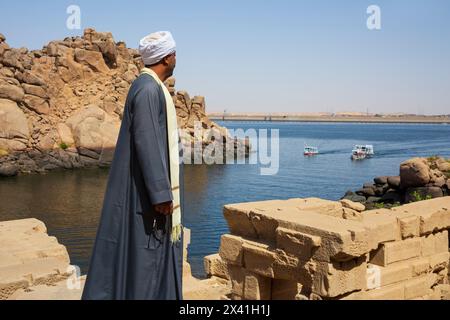 Ein ägyptischer Mann in traditioneller Kleidung, der den Assuan Low Dam (Old Assuan Dam) vom Philae Temple Complex auf Agilkia Island (Nubien) aus betrachtet Stockfoto