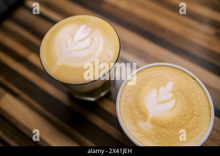 Zwei Tassen Cappuccino mit Blättern auf dem Schaumstoffständer auf einem Holztisch Stockfoto
