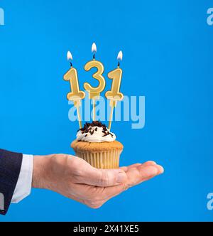 Hand hält einen Cupcake mit der Zahl 131 Kerze - Geburtstag auf blauem Hintergrund Stockfoto