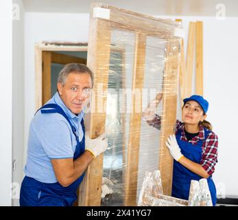 Professionelle Handwerker in Overalls schleppen die Türkonstruktion in eine Wohnung Stockfoto