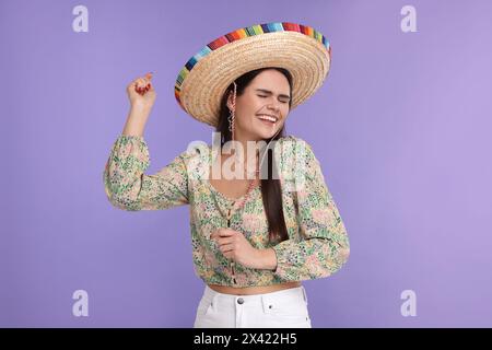Junge Frau mit mexikanischem Sombrero-Hut, der auf violettem Hintergrund tanzt Stockfoto