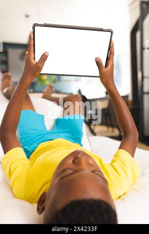 Ein afroamerikanischer Junge, der zu Hause eine Tablette hält, ein gelbes Hemd trägt, einen Kopierraum Stockfoto