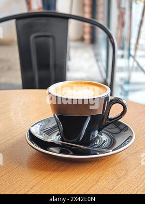 Eine Tasse flacher weißer Kaffee auf einem Holztisch in einem Café. Stockfoto