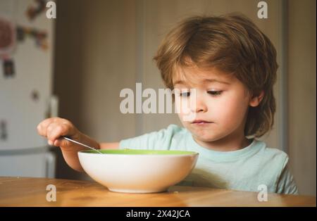 Kinder essen. Porträt des süßen kleinen lachenden Jungen mit blonden Haaren, der vom Tellerlöffel isst - Nahaufnahme. Glücklicher Junge isst gesundes Essen Stockfoto