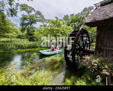 Touristen auf einem kleinen Boot, das an einem alten, traditionellen Wasserrad auf einem kleinen Fluss in Nagano, Japan, vorbeifährt Stockfoto