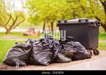 Ein Haufen Plastikmüllsäcke am Straßenrand in der Nähe eines Kunststoffbehälters. Müllsäcke auf der Straße. Schwarze Müllbeutel. Müllbegriff Stockfoto