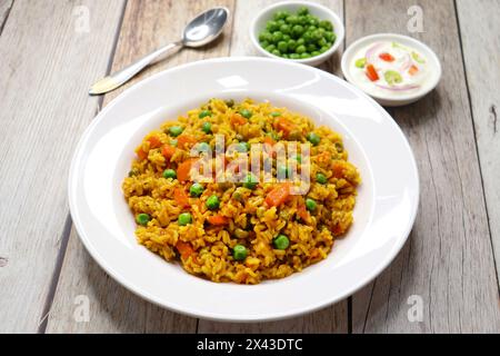 Karotten und Erbsen Pilaf oder Gajar Matar Pulao. Es ist ein eintöniges Reisgericht mit Basmati-Reis und Gemüse, gewürzt mit Gewürzen, serviert mit Joghurt Stockfoto