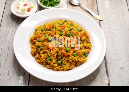 Karotten und Erbsen Pilaf oder Gajar Matar Pulao. Es ist ein eintöniges Reisgericht mit Basmati-Reis und Gemüse, gewürzt mit Gewürzen, serviert mit Joghurt Stockfoto