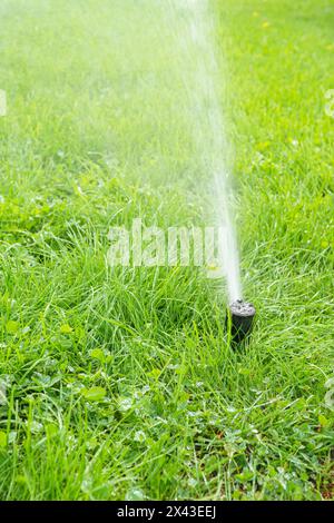 Automatischer intelligenter Rasenregner, der an sonnigen Tagen grünes Rasengras bewässert. Sprinkler mit automatischer Anlage mit verstellbarem Kopf, Gartenbewässerungsanlage. Stockfoto