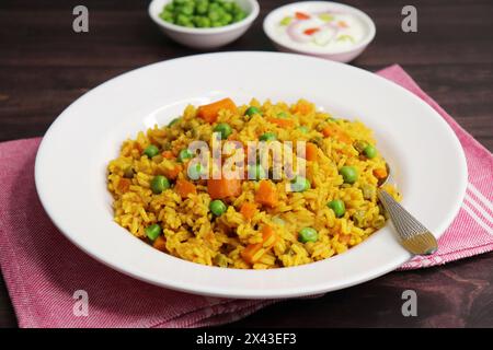 Karotten und Erbsen Pilaf oder Gajar Matar Pulao. Es ist ein eintöniges Reisgericht mit Basmati-Reis und Gemüse, gewürzt mit Gewürzen, serviert mit Joghurt Stockfoto