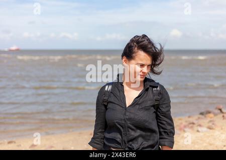 Porträt einer schönen brünetten Frau, die schwarze Kleidung auf dem Hintergrund des Meeres trägt Stockfoto