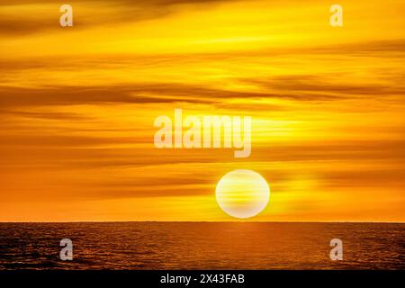 Das goldene Licht des Sonnenuntergangs in den wirbelnden Wolken reflektiert ein rosafarbenes Leuchten am Strand von Pererenan, Bali, Indonesien Stockfoto