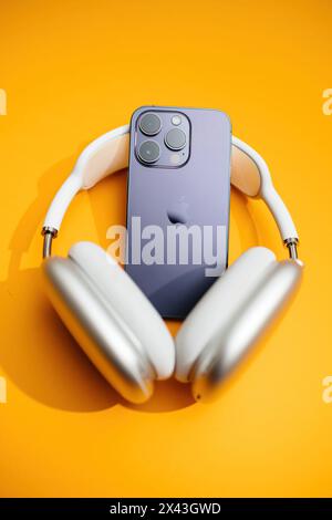 Paris, Frankreich – 29. September 2022: Ein iPhone Pro mit luxuriösen Ohrstöpseln Max Headphones vor leuchtendem orangefarbenem Hintergrund Stockfoto