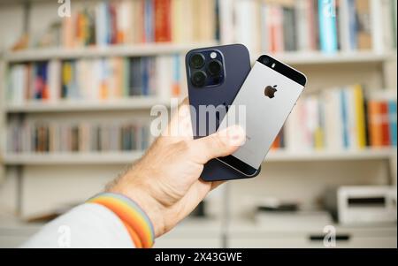 Paris, Frankreich, 29. September 2022: Hand mit dem iPhone 14 Pro über einem iPhone SE vor dem Hintergrund eines Bücherregals Stockfoto