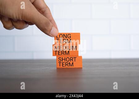 Hand Pick Holzwürfel mit Text LANGFRISTIG auf blauem Hintergrund mit Kopierraum. Investitionskonzept. Stockfoto