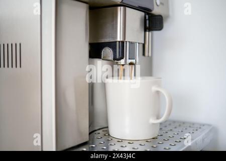 Kaffee wird aus einer Kaffeemaschine in eine Tasse gegossen, Nahansicht Stockfoto