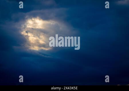 Eindrucksvolles Bild, das Sonnenlicht einfängt, das durch eine dramatische Wolkendecke durchdringt und ein Gefühl der Hoffnung und Offenbarung in einem dunkelblauen Himmel darstellt. Stockfoto