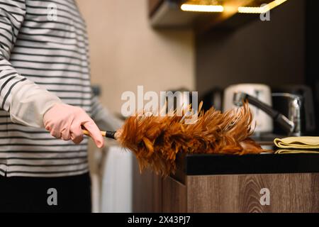 Nahaufnahme eines Mannes, der die Küche mit einem Federstaub bestäubt. Konzept der allgemeinen Ordnung und Sauberkeit Stockfoto