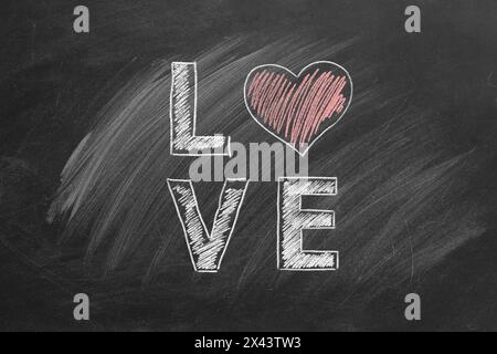 Kreidebuchstaben, in denen LIEBE geschrieben wird, mit einem Herz, das das auf einer Tafel skizzierte O ersetzt. Stockfoto