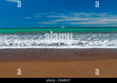 Sanfte Brandung an einem Sandstrand. Das Star Flyer Segelkreuzfahrtschiff in der Ferne. Drake Bay, Osa Peninsula, Costa Rica. Stockfoto
