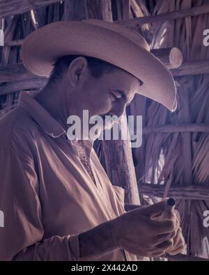 Ein Infrarotbild eines Tabakbauers, der in einer der Trockenställen auf Benito’s Tobacco Farm in Vinales, Kuba, eine Zigarre raucht. Stockfoto