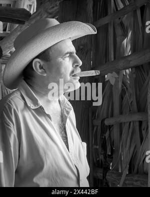 Ein Infrarotbild eines Tabakbauers, der in einer der Trockenställen auf Benito’s Tobacco Farm in Vinales, Kuba, eine Zigarre raucht. Stockfoto