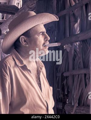 Ein Infrarotbild eines Tabakbauers, der in einer der Trockenställen auf Benito’s Tobacco Farm in Vinales, Kuba, eine Zigarre raucht. Stockfoto