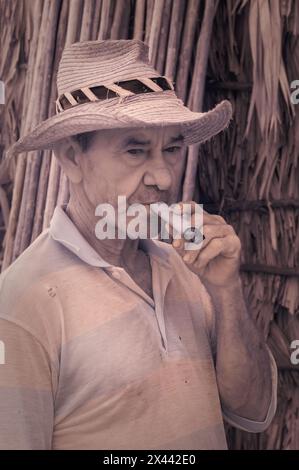 Ein Infrarotbild eines Tabakbauers, der vor einer der Trockenställen in Benito’s Tobacco Farm in Vinales, Kuba, eine Zigarre raucht. Stockfoto