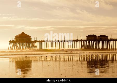 Der Huntington Beach Pier und Surfer bei Sonnenuntergang. Huntington Beach, Kalifornien. Stockfoto