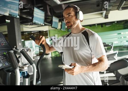 Aktiver Mann in Turnkleidung, der auf dem Laufband joggt, während er über Kopfhörer in Musik eingetaucht ist. Stockfoto