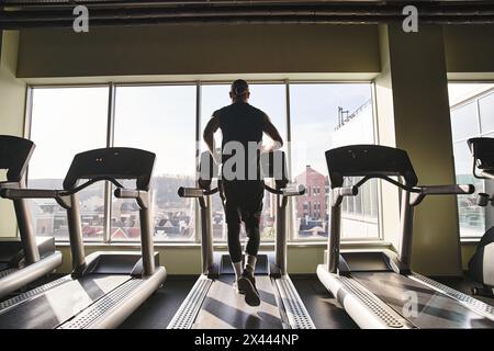 Ein fitter Mann in Activewear läuft in einem Fitnessstudio auf einem Laufband und setzt sich in seine Trainingsroutine ein. Stockfoto
