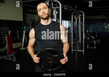 Ein sportlicher Mann in aktiver Kleidung, der beim Training im Fitnessstudio eine schwarze Platte hält. Stockfoto