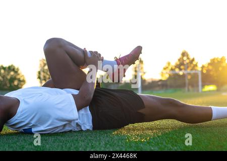 Nahaufnahme eines auf dem Boden liegenden lateinischen Fußballspielers, der sich über eine Fußballverletzung beschwert Stockfoto