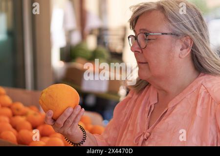 Ältere weißhaarige Frau, die Orangen auf einem Straßenmarkt kauft Stockfoto
